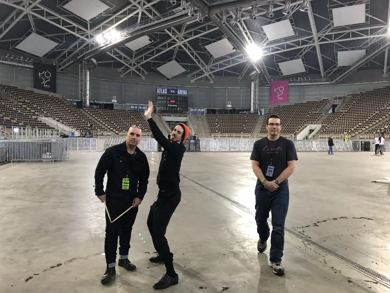 Three people on the floor of an empty arena under the lighting rig