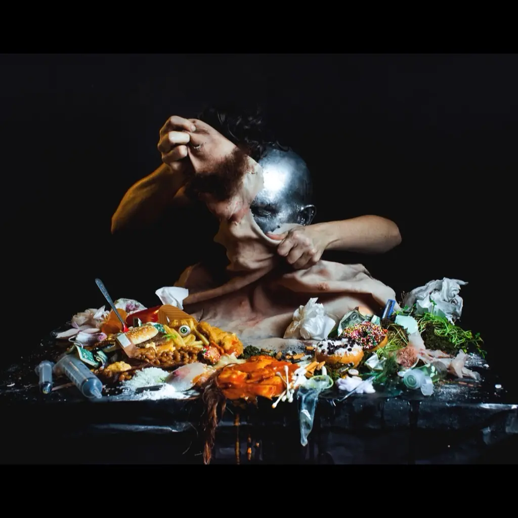 A sculpted figure pulling at its face over a table piled with food