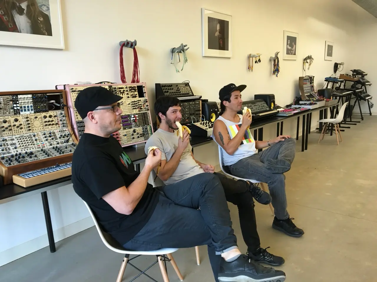Three men eating bananas in a gallery of modular synths