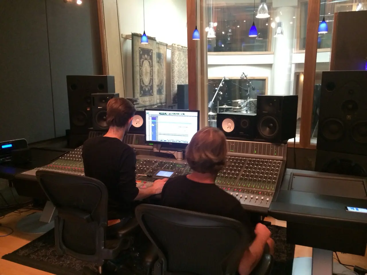 Two people at a large mixing console and screens in a control room