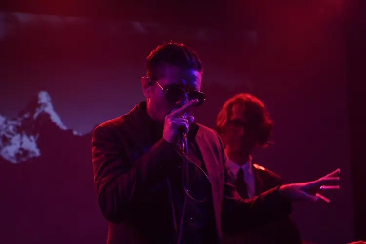 A singer in sunglasses under red light, a second performer behind
