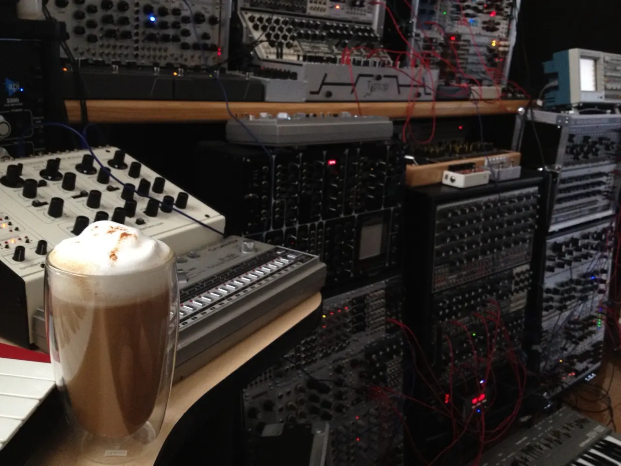 A coffee in a glass mug in front of racks of modular synth