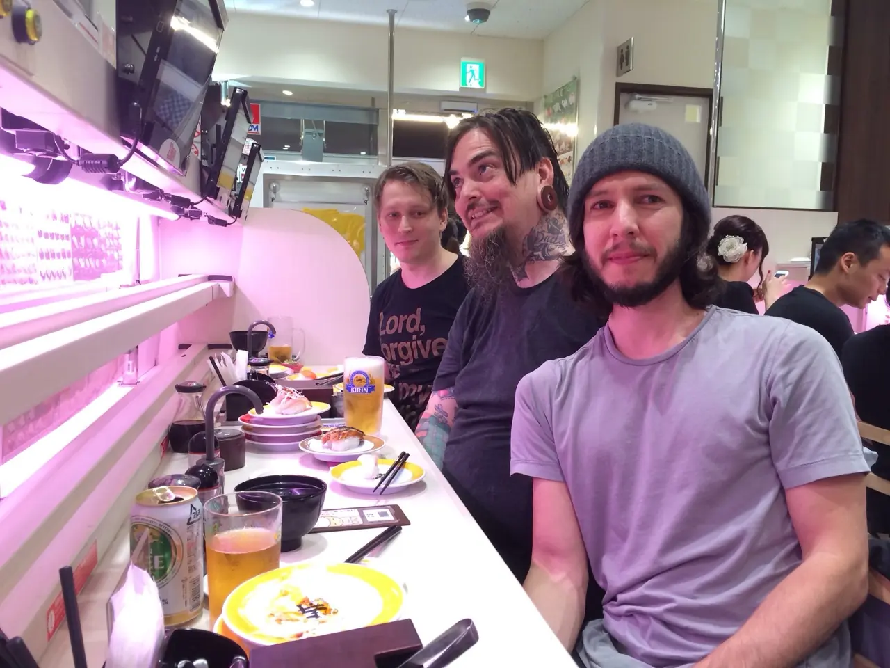 Three men at a restaurant counter under pink light