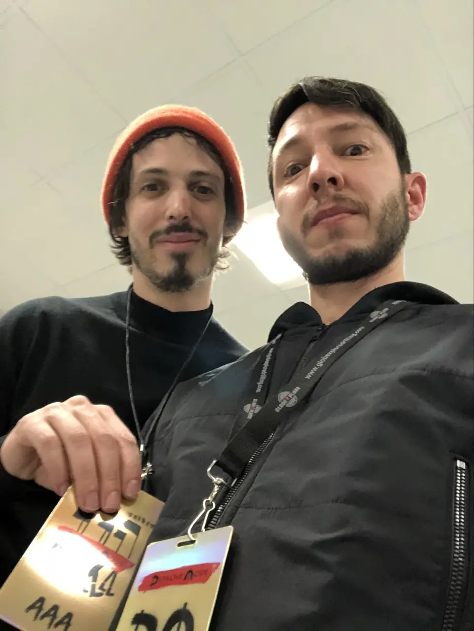 Two men in a selfie, holding up tour laminates