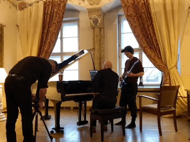 A session by a grand piano in a room with tall curtains, a camera on a tripod