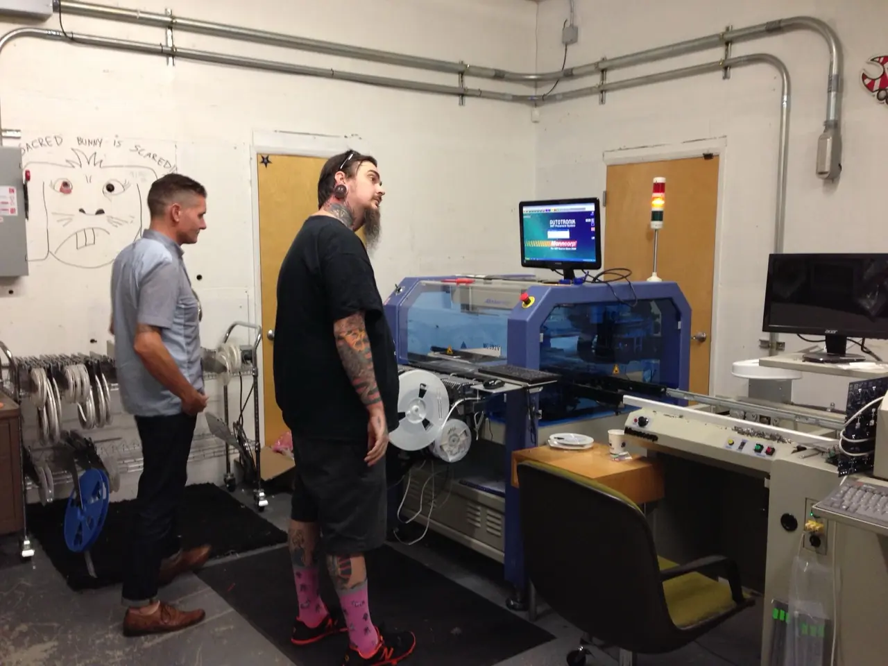Two men by a surface-mount assembly machine on a factory floor