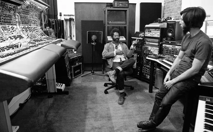 Black and white: Robert Aiki Aubrey Lowe (Lichens) seated in the Los Angeles studio, talking with a man leaning on the desk