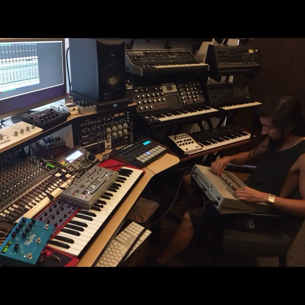 Baseck at a desk stacked with synths and keyboards